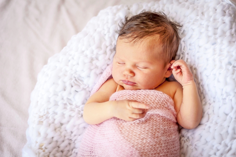 Cute Caucasian newborn infant baby girl asleep wrapped in a soft pink plaid. 