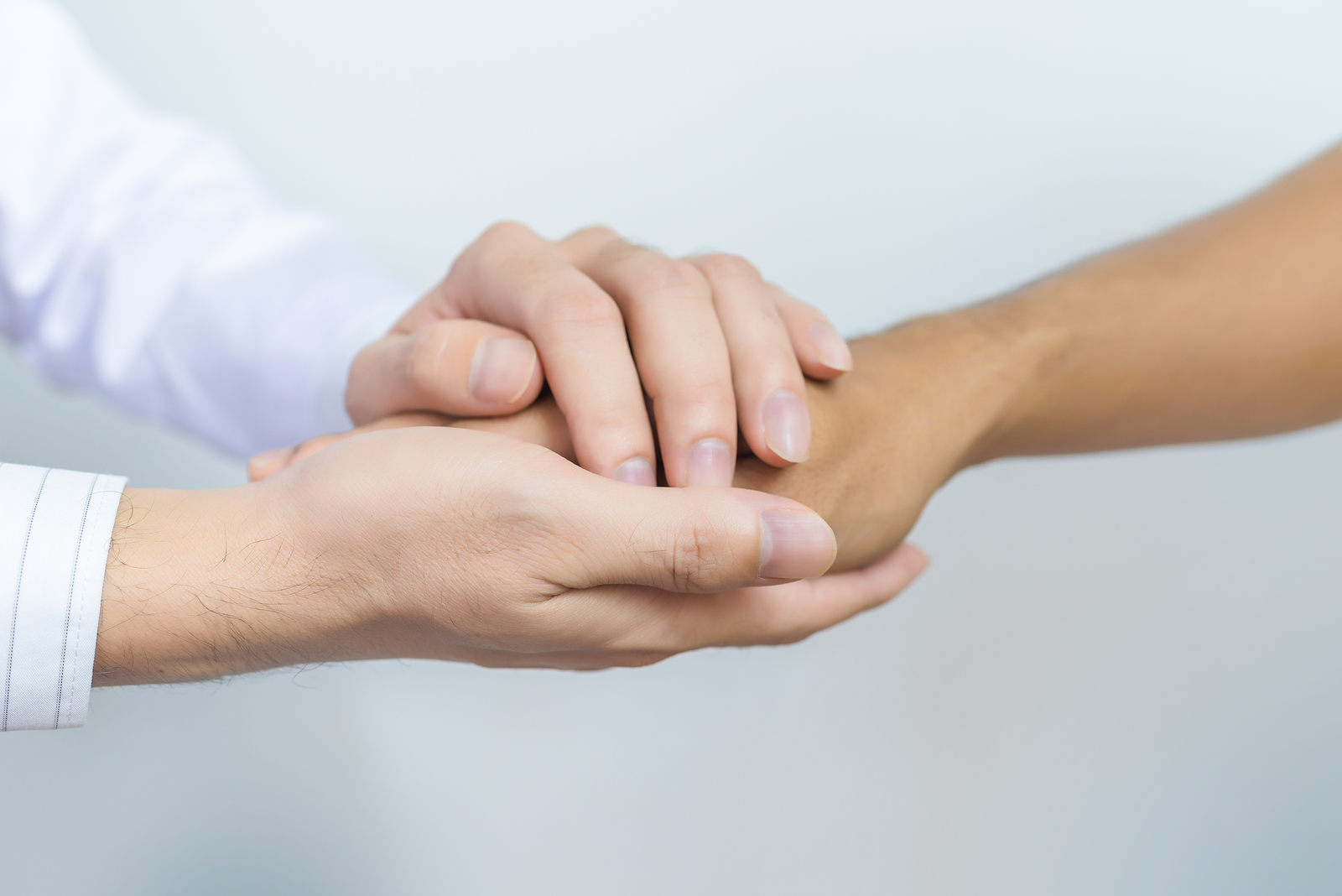 Two people holding hands for comfort. Doctor consoling relatives of patients in hospital concept.