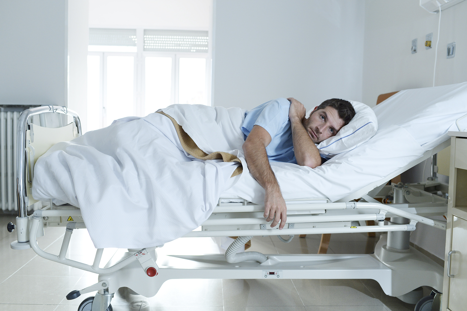 young desperate man sitting at hospital bed in fear about health