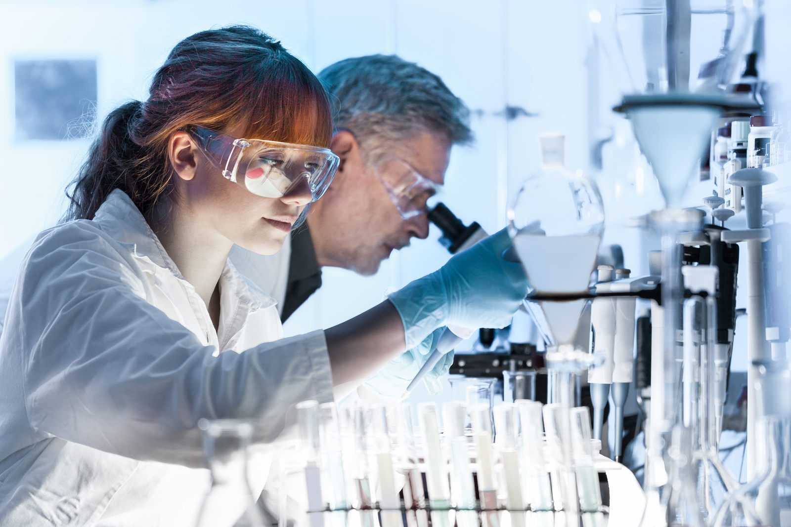 Young female research scientist and senior male supervisor preparing and analyzing microscope slides in research lab