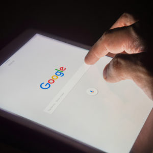 A man's hand is touching screen on tablet at night for searching on Google search engine. Google is the most popular Internet search engine in the world.