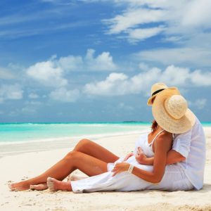 Happy man in love giving piggyback ride to smiling woman at the beach. Couple enjoying vacation at beach with copy space. Banner of summer young couple in a tropical beach