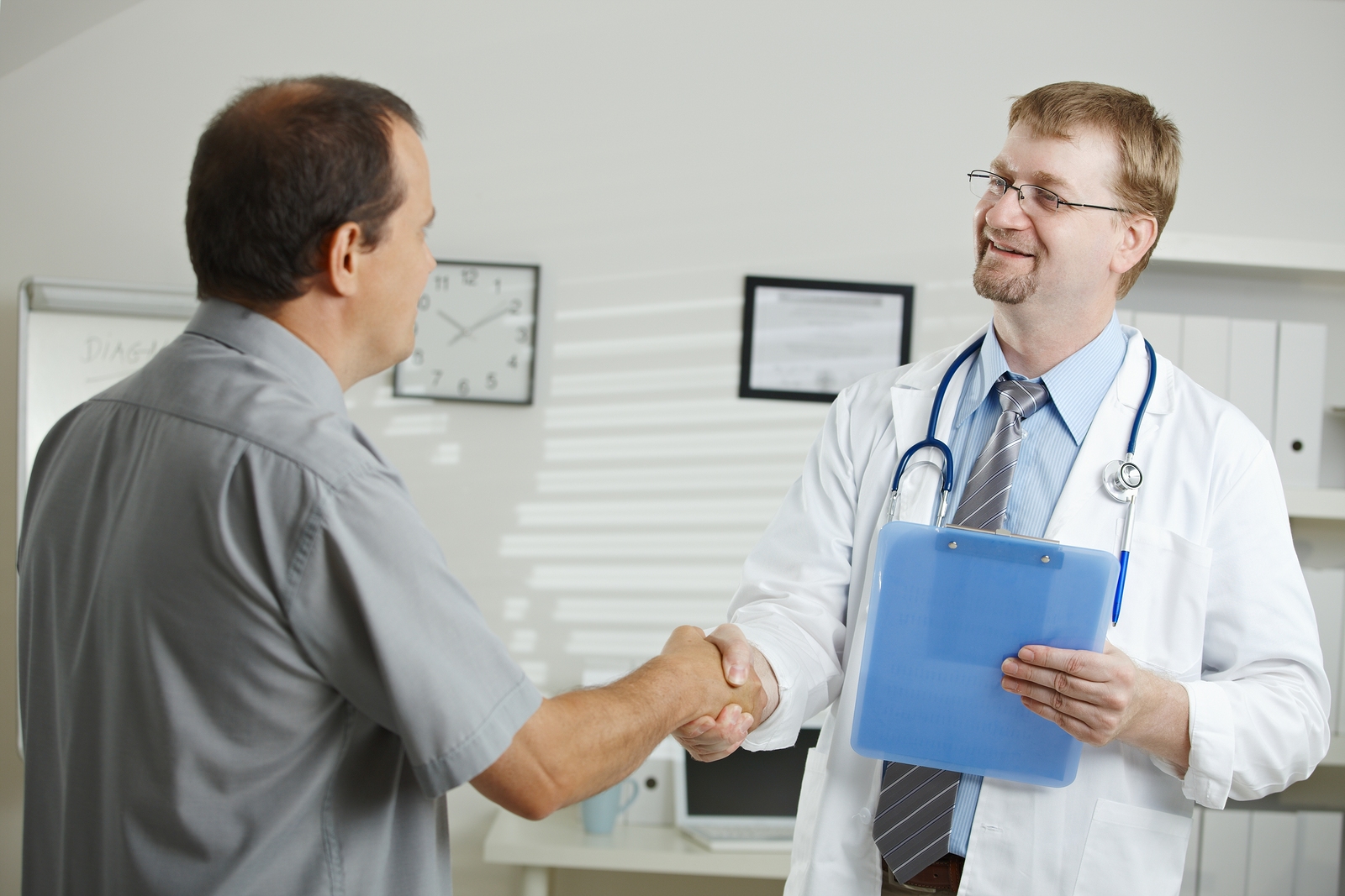 Medical office - middle-aged male doctor greeting patient, shaking hands.