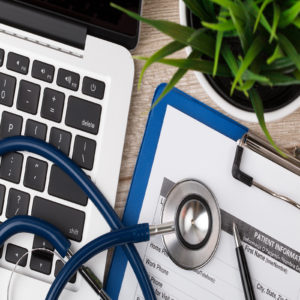 Close-up view of medical doctor’s working table. Laptop stethoscope and patient information form.