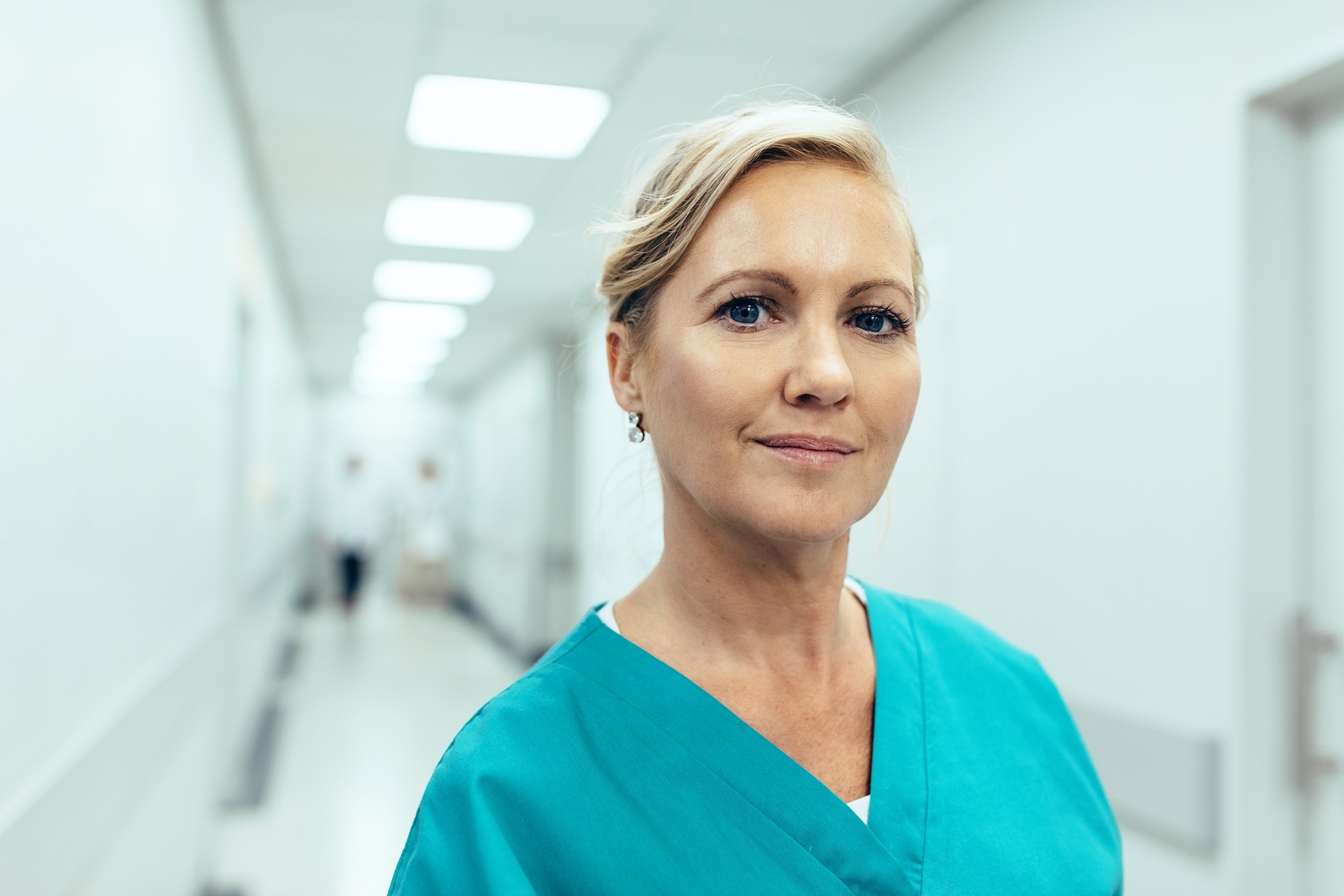 Close up portrait of female healthcare worker standing in hospital corridor. Caucasian woman in hospital hallway staring at camera.